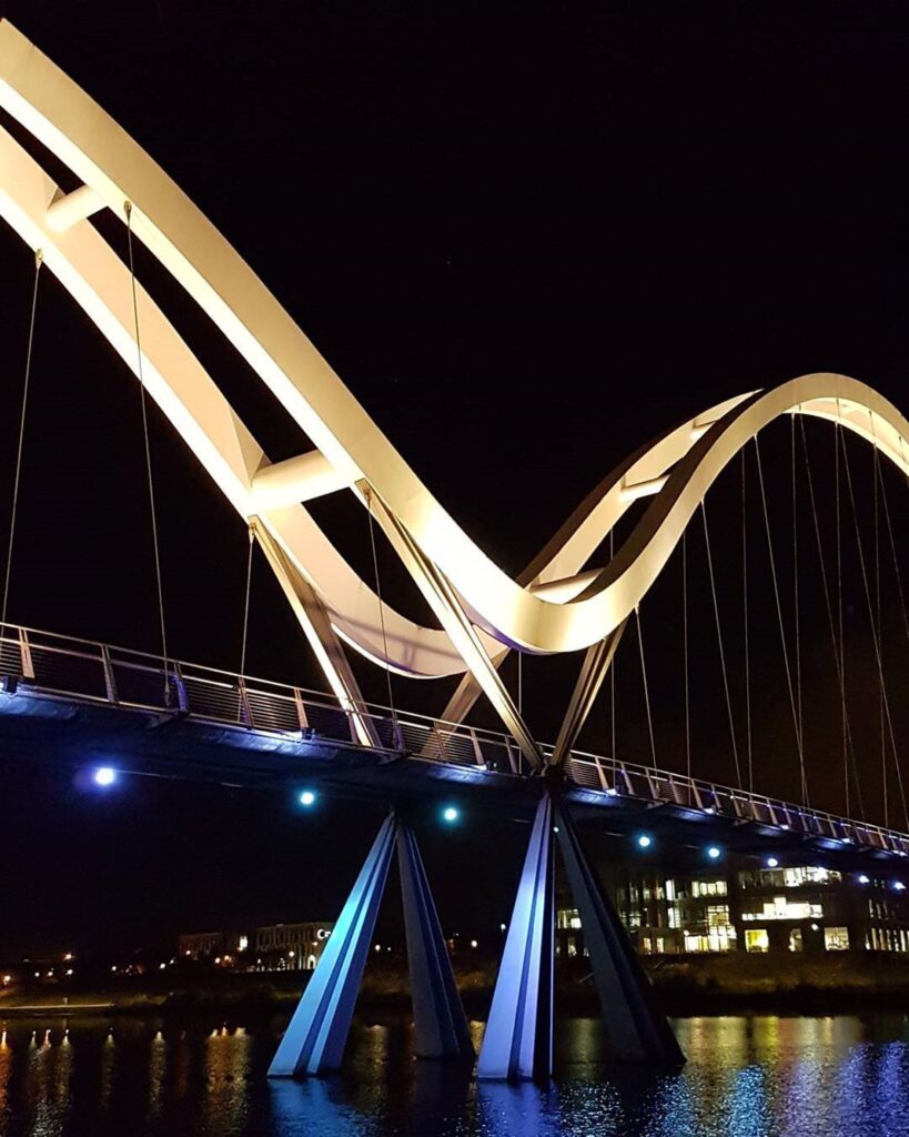 Dramatic night view of the illuminated Infinity Bridge spanning calm river in Stockton-on-Tees.