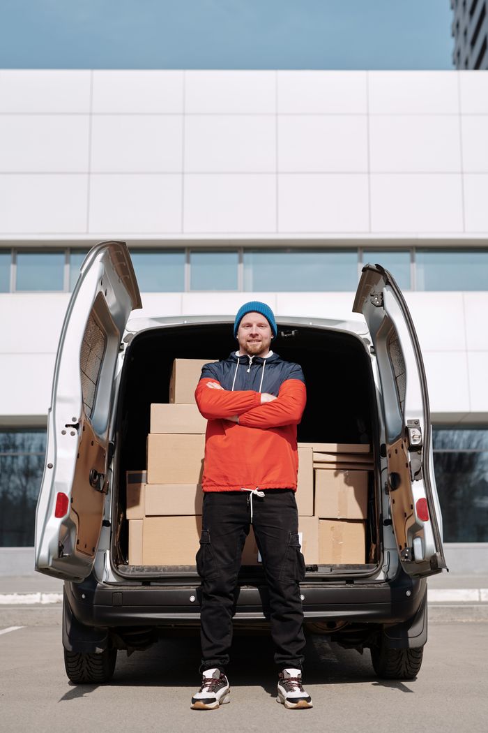 Confident delivery man poses with cardboard boxes in an urban setting.